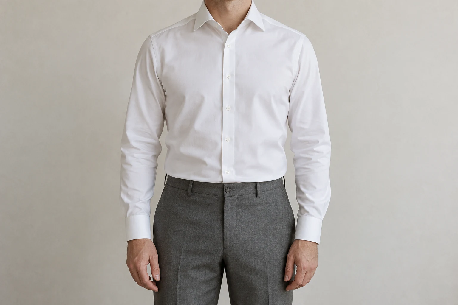 A man shown from the neck down wears a white poplin shirt tucked neatly into gray trousers.