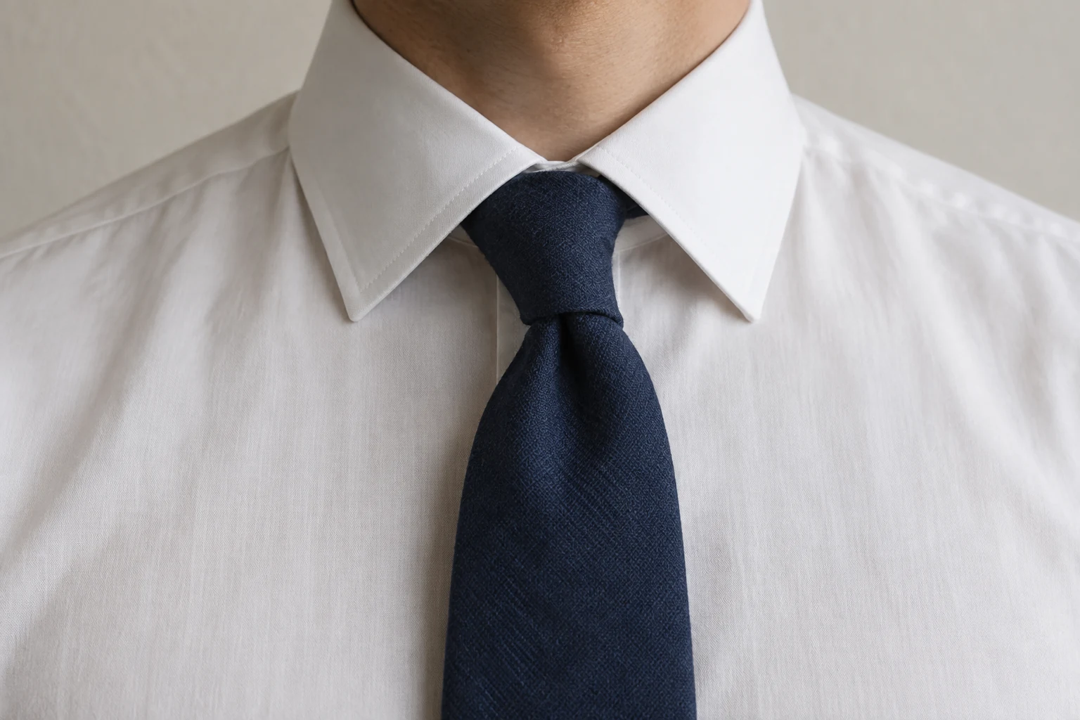 A navy textured tie forms a slightly leaning four in hand knot under a crisp white point collar