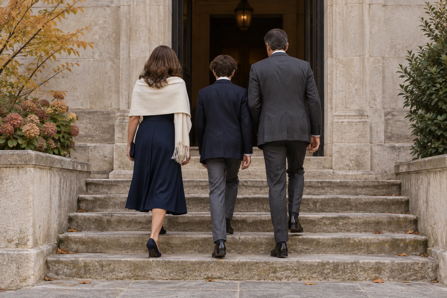 A formally dressed family walks up stone steps toward a quiet entrance on an autumn morning.